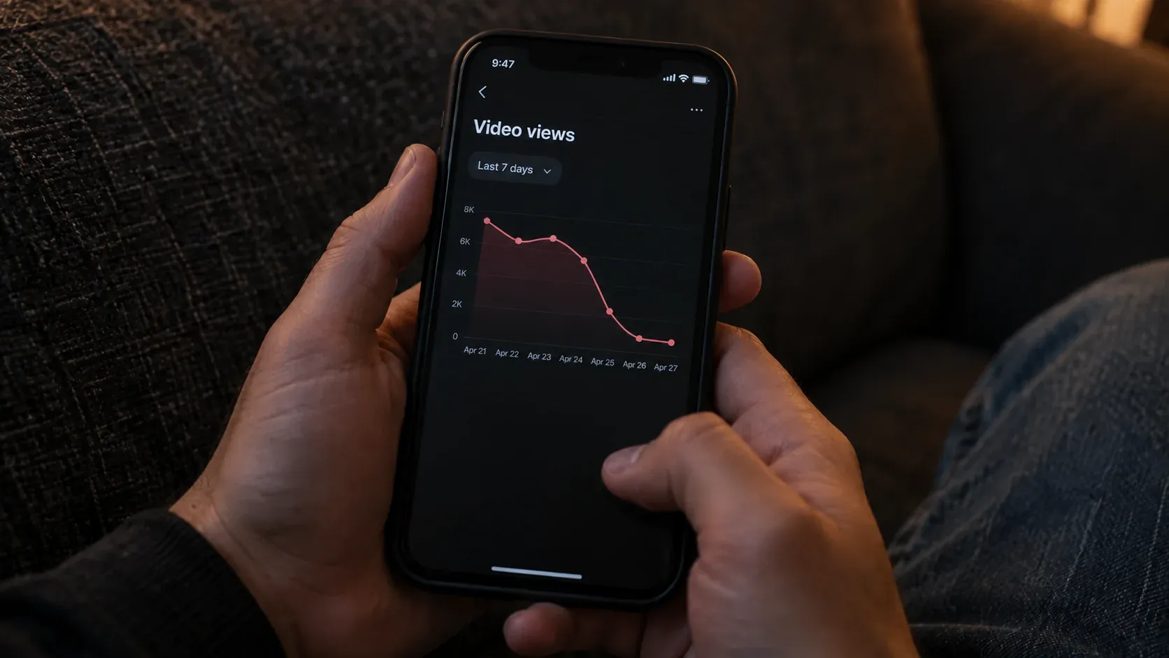 Close view of hands holding a phone with a declining video views chart in a dimly lit room